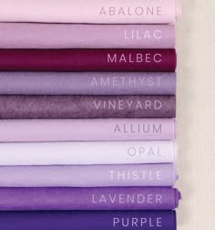 a collection of fabric swatches, arranged in order from pale pink to deep purple. each swatch has a different name written on it,  including "abalone", "lilac", "malbec", "amethyst", "vineyard", "allium", "opal", "thistle", "lavender", and "purple".