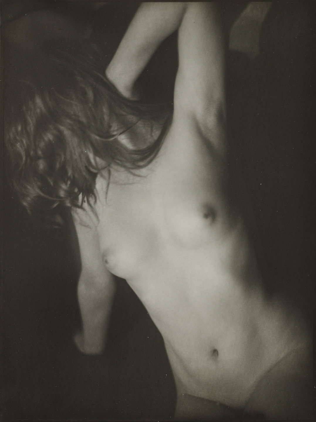 the image is a black and white closeup photograph of a nude female torso. the woman's body is angled, and her long, wet hair partially obscures her face. her left arm is raised above her head, and her right arm is bent at the elbow. the lighting is dramatic, using shadows to create contrast and emphasize the contours of the body. the overall mood of the photograph is sensual and intimate, and there is a suggestion of a quiet intimacy within the dark setting.  the image's focus is on the texture and form of the body, emphasizing the interplay of light and shadow.