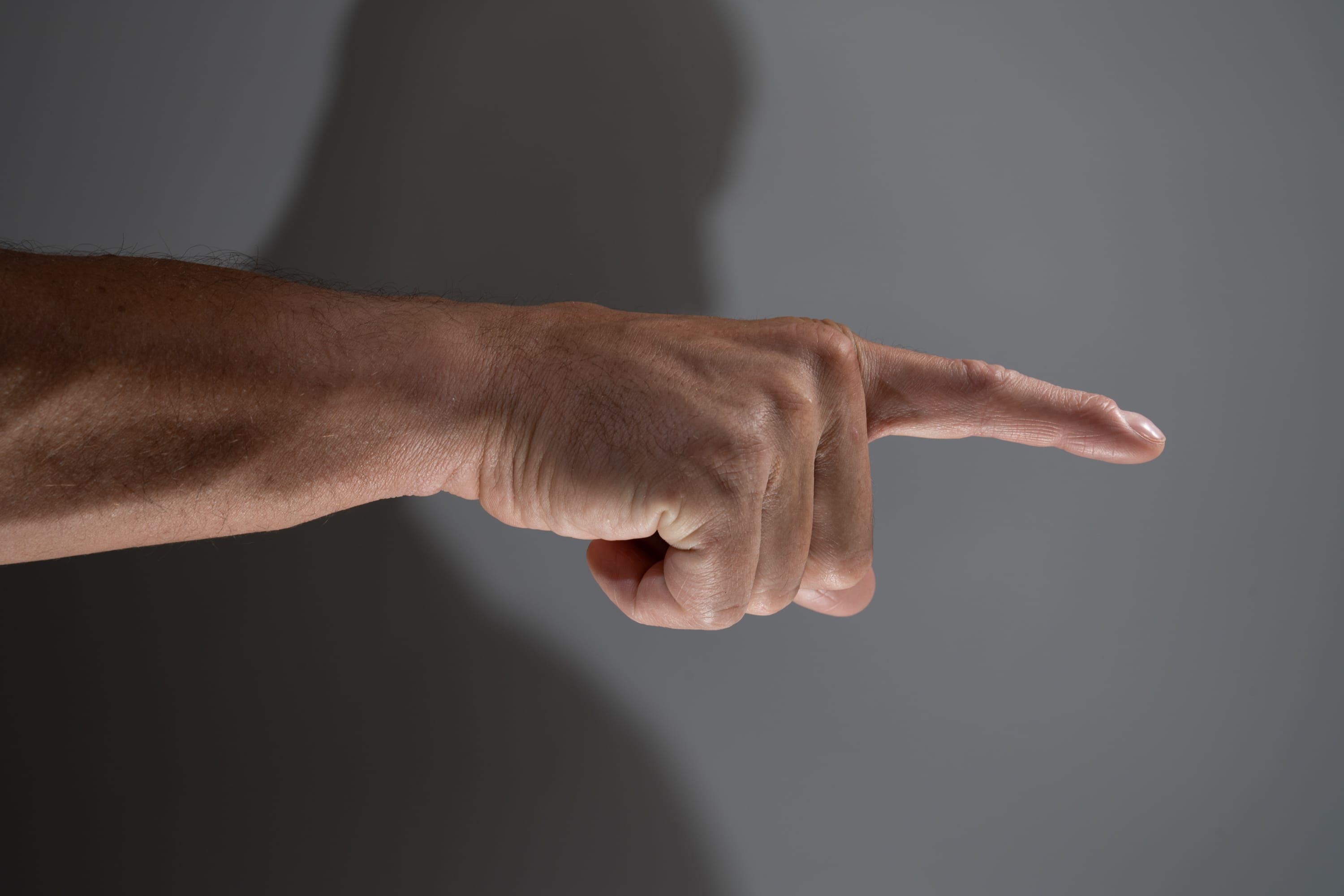 a closeup image of a man's arm and hand pointing towards the right. the image uses strong sidelighting to create dramatic shadows on the background.