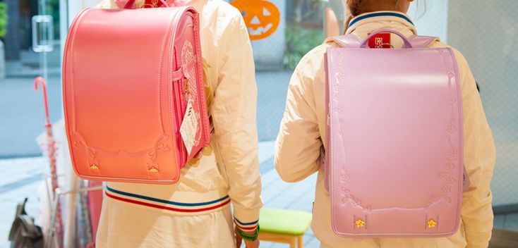 two children are wearing backpacks. the backpack on the left is pink and the backpack on the right is purple. they are wearing school uniforms.