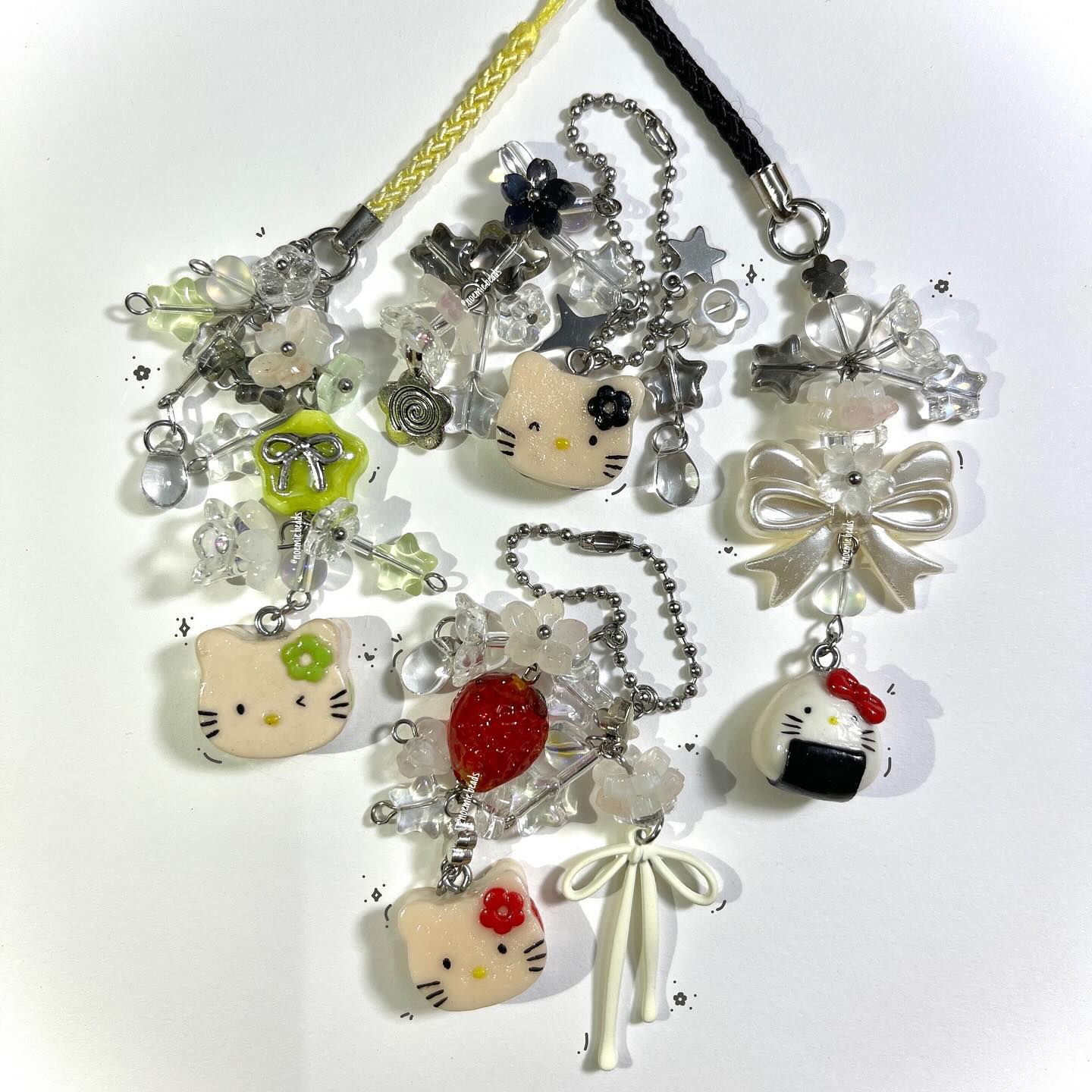 the image shows a collection of handcrafted keychains with a kawaii aesthetic. each keychain features a hello kitty charm with different flower details, along with various beads, including clear and pastelcolored ones. other charms include a red strawberry, an onigiri, bows, flowers, and stars. the keychains are attached to either yellow or black straps with silver hardware. the overall style is cute, handmade, and unique, indicating they are likely handmade jewelry.