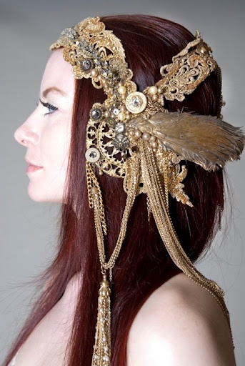 a woman with long, red hair is wearing a gold headpiece with chains and beads. the headpiece is very intricate and ornate. the woman has a simple background that allows the headpiece to be the focus of the image.