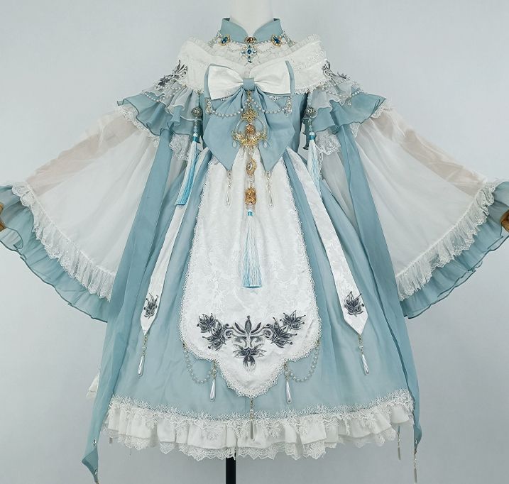 the image shows a light blue and white lolita fashion dress. the dress has a high collar, long sleeves with ruffles, and a full skirt. it is decorated with embroidery, lace, and a large bow. the dress is shown on a mannequin in a studio setting.