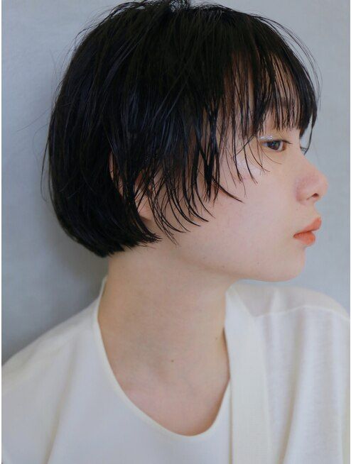 closeup portrait of a young woman with short black hair. she is wearing a plain white shirt. her hair is styled in a simple, straight style, with a few strands framing her face. she is looking away from the camera. the photo is taken against a plain white background.