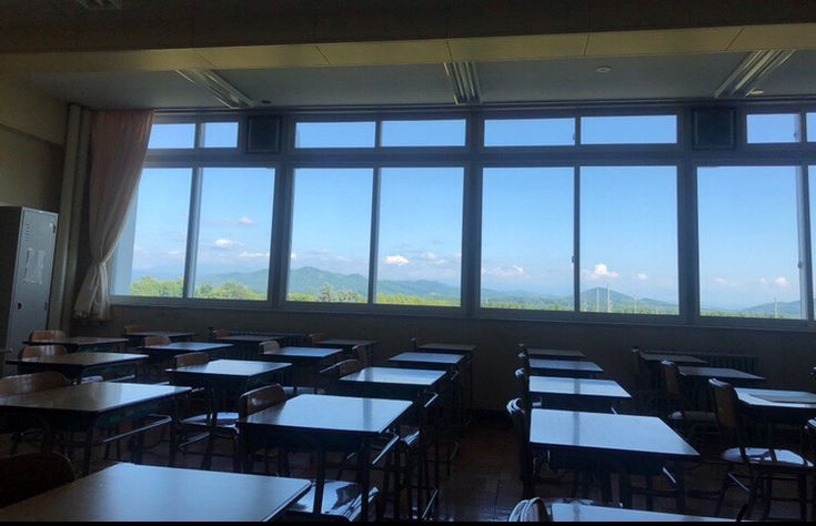 the image shows an empty classroom with rows of desks and chairs.  a large window spans the length of the room, offering a panoramic view of a serene mountain landscape under a clear blue sky. the overall atmosphere is peaceful and quiet. the classroom appears clean, simple, and wellorganized.  the lighting suggests it is daytime.