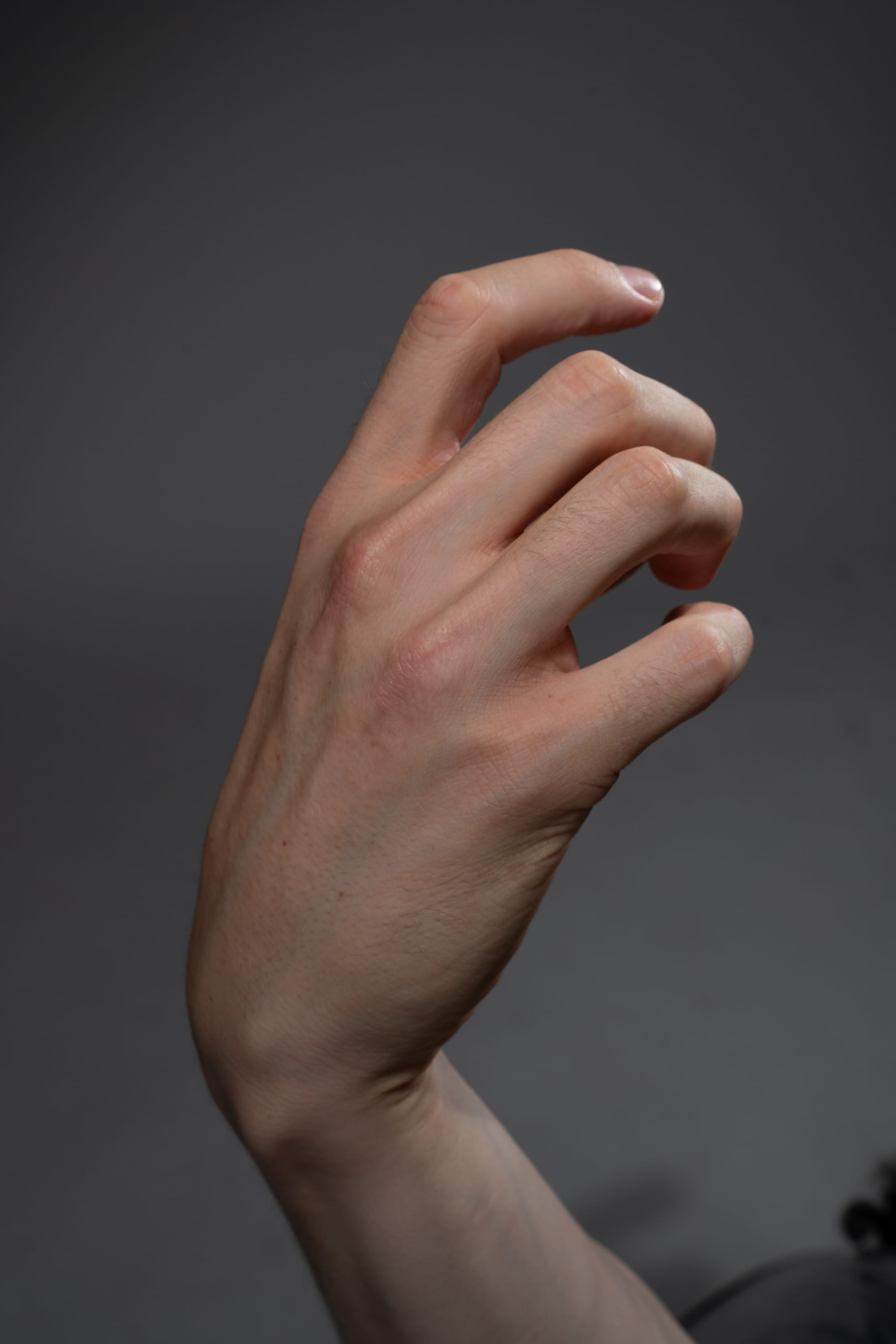 a closeup view of a human hand with its fingers partially curled inwards, set against a plain gray background. the studio lighting accentuates the details of the hand, showcasing its texture, wrinkles, and natural curvature. the hand, likely belonging to a fairskinned individual, exhibits a soft, diffused reflection of the light. the overall image conveys a sense of stillness and simplicity, emphasizing the intricate form of the human hand.