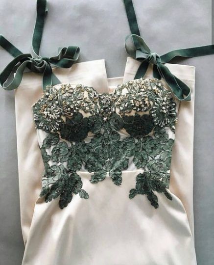 loseup view of an elegant, creamcolored jumpsuit or dress. the bodice features intricate sage green embroidered lace appliques with beaded embellishments. the straps are long and tied in bows, made of a dark green fabric that matches the embroidery. the overall style is formal and luxurious, suitable for a wedding, party or other special occasion. the fabric appears to be satin or silk, giving it a smooth and sophisticated look.