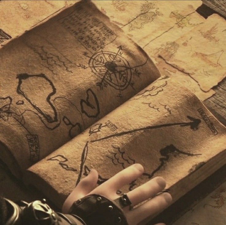 an open, aged book containing a treasure map rests open on a surface, with a hand adorned with a ring and leather bracer gesturing towards the maps. the map is drawn on a tan, aged parchment, depicting various landmarks, a compass rose, and route lines. additional parchment scraps with similar map drawings are visible in the background, alluding to a theme of adventure and navigation.