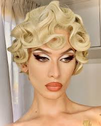 closeup portrait of a blonde woman with meticulously styled 1920s1930s finger waves.  her makeup is glamorous and complements the vintage hairstyle. she is wearing minimal jewelry, and her shoulders and neck are visible.  the background is blurred, drawing focus to the subject. the overall impression is one of classic beauty and elegance.