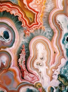 a closeup image of a colorful agate slice with a complex pattern of veins and swirls. the agate is cut and polished to reveal its intricate structure. the colors are rich and vibrant, ranging from deep reds and oranges to soft pinks and creams. the agate has a wavy and swirling pattern, creating an abstract and mesmerizing image. the texture of the agate is smooth and polished, with a slight sheen.
