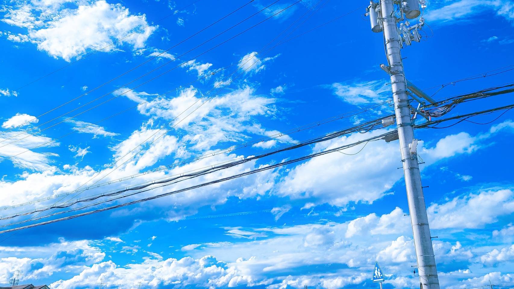 the image shows a view looking up at a bright blue sky filled with fluffy white clouds. power lines run diagonally across the frame, connected to a tall utility pole on the right side. the overall impression is one of a clear, sunny summer day.