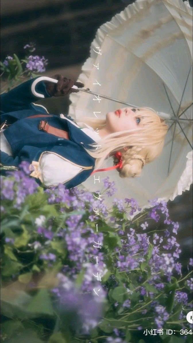 a young woman in a violet evergarden cosplay poses amidst a field of purple flowers. she holds a white lace parasol and wears a dark blue dress, evoking the character's refined appearance. the image is soft and dreamy, with a pastel color palette that complements the cosplay and setting. the overall atmosphere is romantic and whimsical, like a scene from a fairytale.