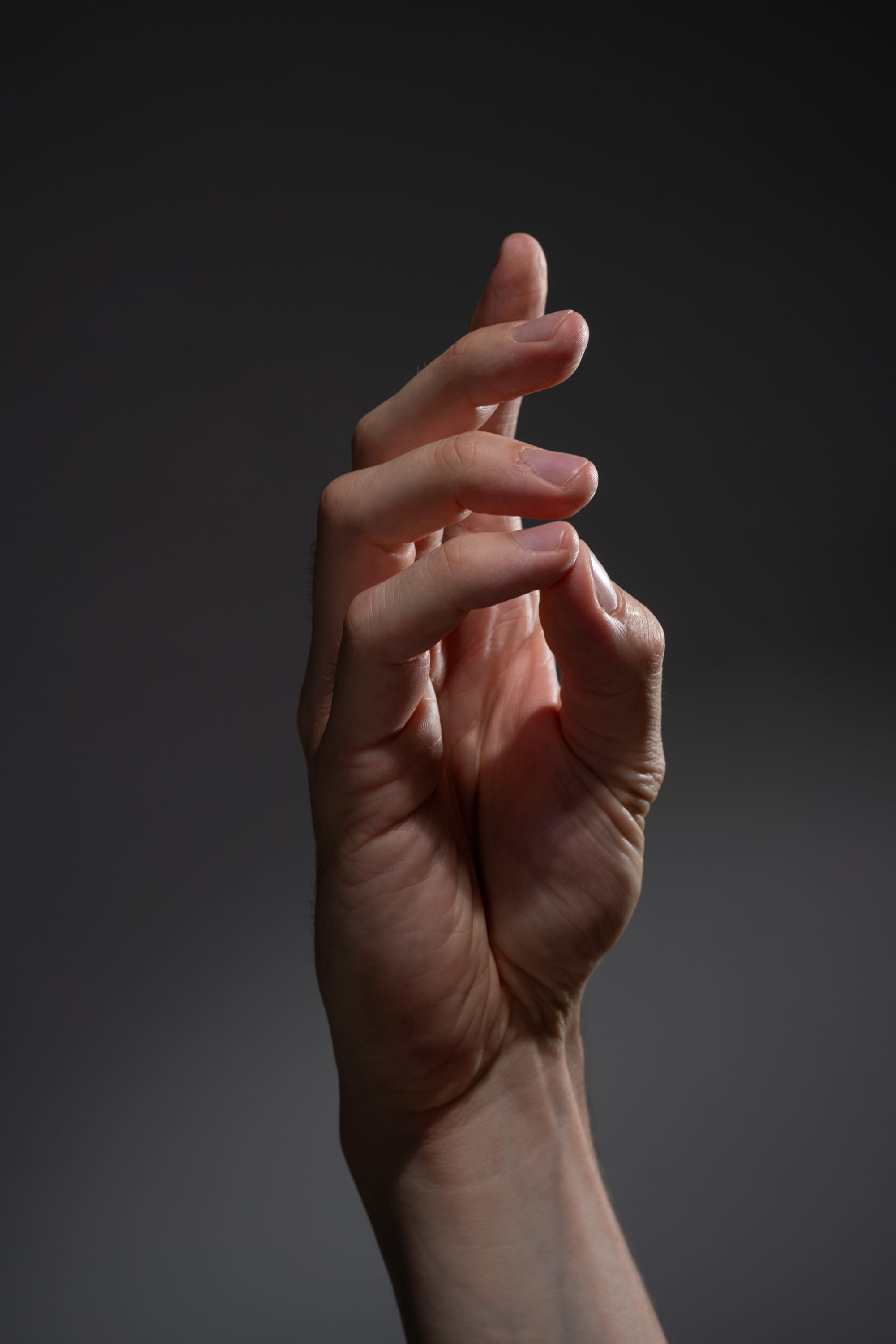 the image is a closeup shot of a male hand against a dark gray background. the hand is extended, with the fingers slightly curled inward. the studio lighting creates a dramatic effect, highlighting the details of the hand's anatomy.
