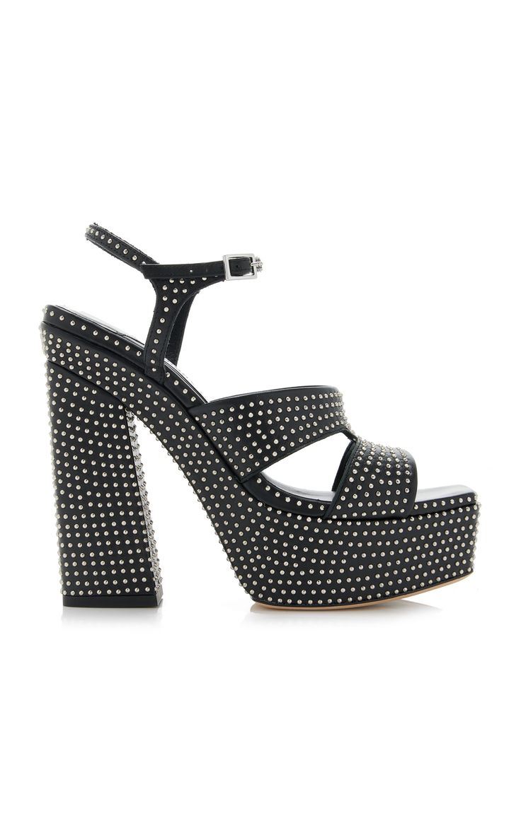 a pair of black studded platform sandals are shown in the image.  the sandals are made of black leather and have a chunky platform heel. they have silvertoned studs covering the entire shoe and an ankle strap with a buckle closure. the shoes are angled slightly to the left.  the background is plain white, and the focus is sharply on the shoes.