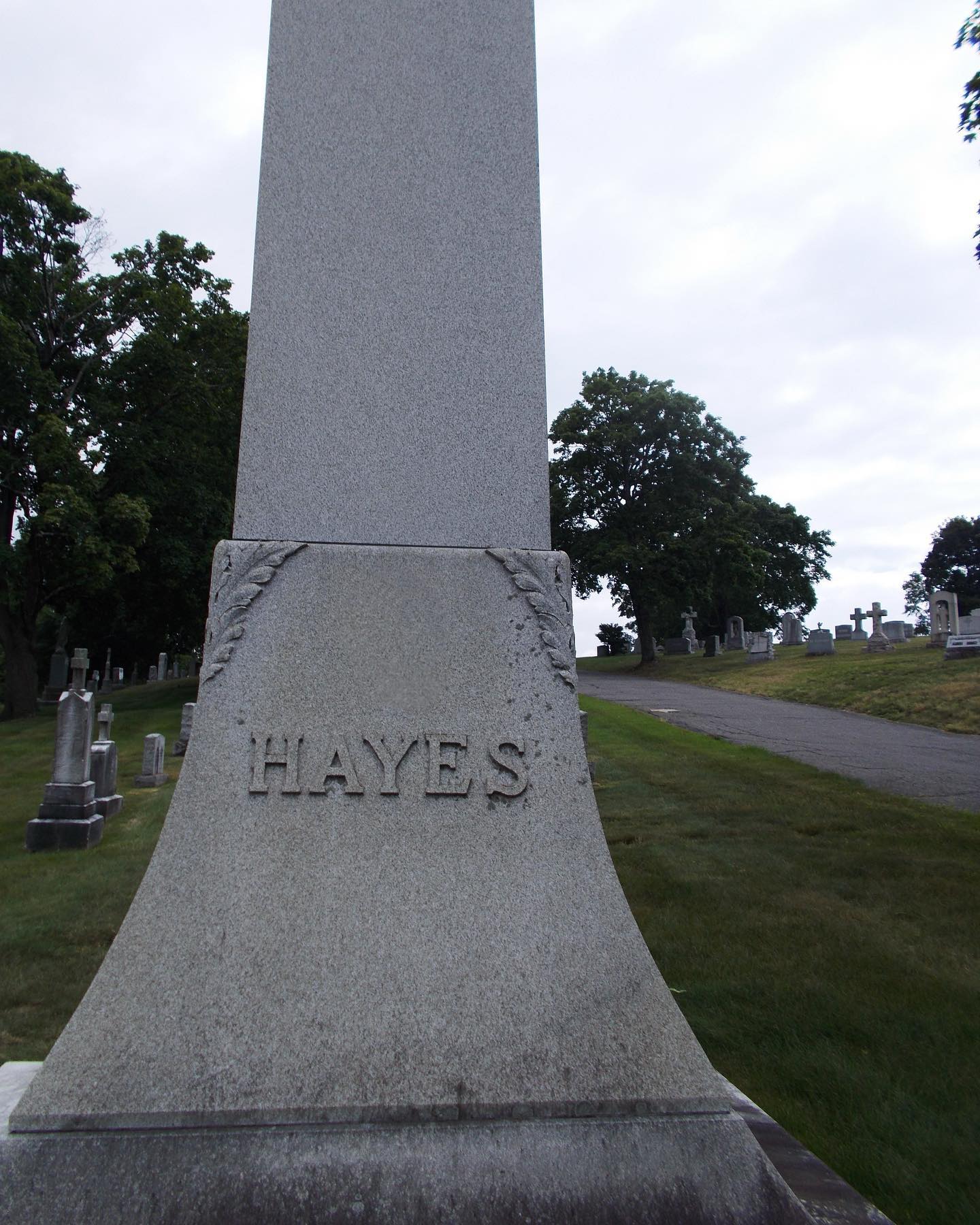 the image shows a large gray gravestone in a cemetery. the name "hayes" is carved into the stone. there are trees and grass in the background.