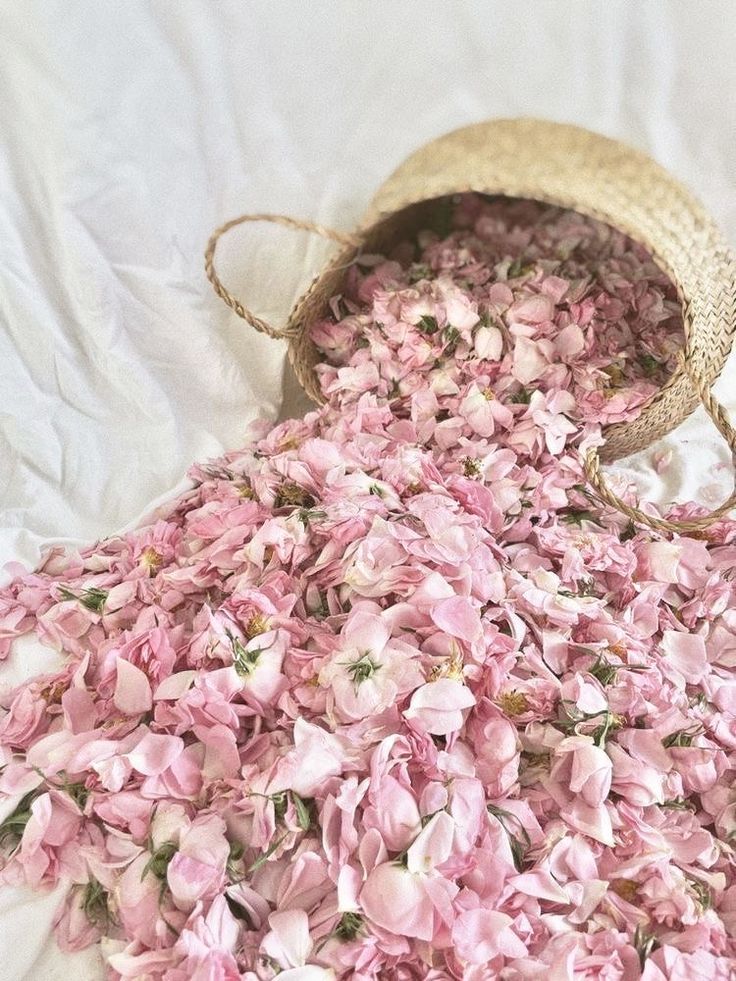 a wicker basket is tipped over, spilling dried pink rose petals onto a white cloth. the petals are scattered widely around the basket.