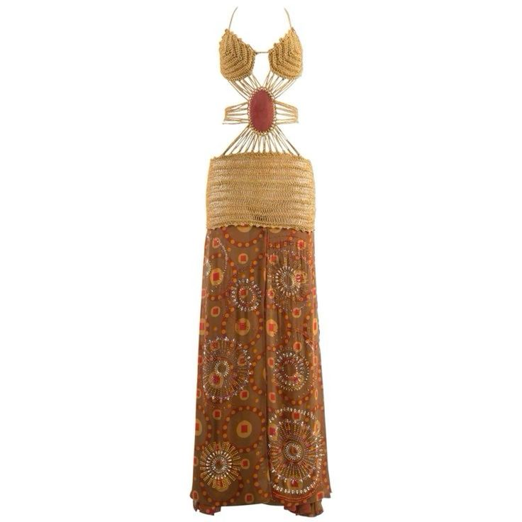 the image shows a bohemianstyle maxi dress. the dress features a halter top with crocheted or woven details and an open back with a large gemstone detail in the center. the upper part of the dress, around the waist, is made of woven straw. the skirt of the dress is brown with ethnicinspired circle patterns, with sequin and bead accents.