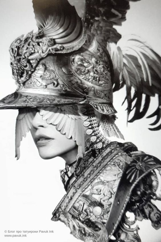 a striking black and white photographic portrait of a woman styled as a warrior. she wears an elaborate, ornate helmet adorned with feathers, and her expression is both powerful and elegant. the image evokes a sense of strength, beauty, and drama.