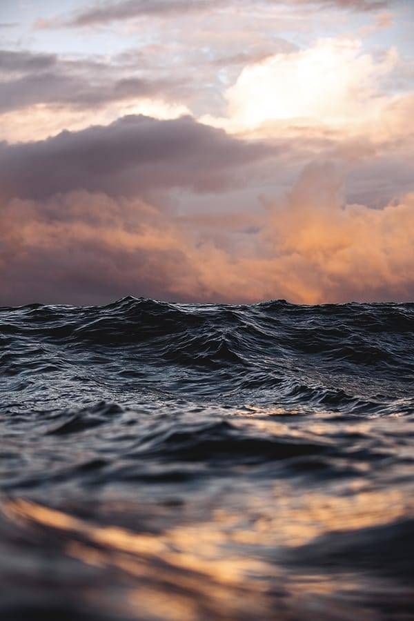 a stunning sunset over the ocean. the sky is ablaze with vibrant colors of orange, pink, and purple, as the sun dips below the horizon. the water is calm and reflective, reflecting the colors of the sky. the waves are gently rolling, creating a sense of tranquility and peace.