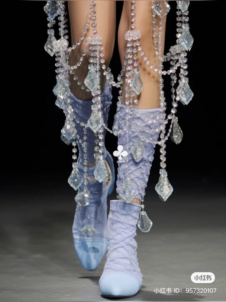 the image shows a closeup of two legs wearing blue shoes with beads hanging down.