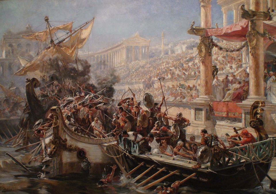 this painting depicts a naval battle in ancient rome. ships are engaged in combat, with soldiers fighting with spears and shields. a large crowd watches from an amphitheater, with the emperor and spectators seated in a prominent box. there is fire and smoke from the battle, and the backdrop shows roman architecture, including columns and a palace.