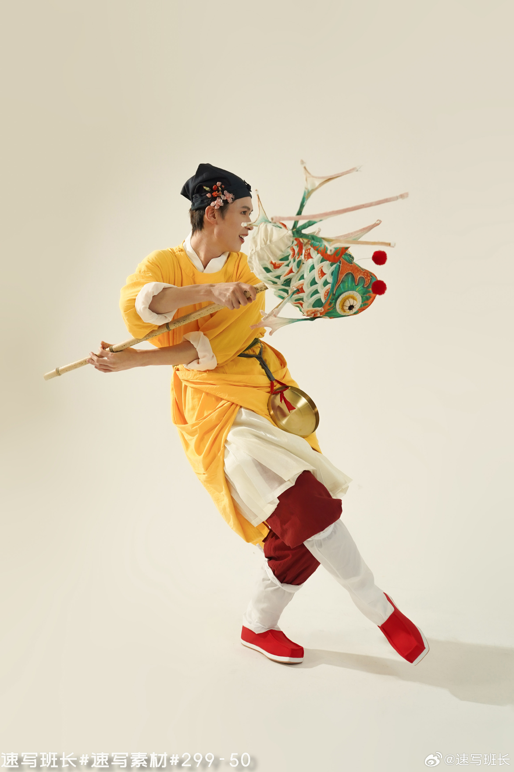 a male dancer, dressed in a traditional bright yellow chinese costume, performs with a large ornate kite prop. he leaps through the air with a joyful expression as he manipulates the kite with a wooden rod. the image is taken in a studio setting with bright lighting, creating a clean and crisp aesthetic.