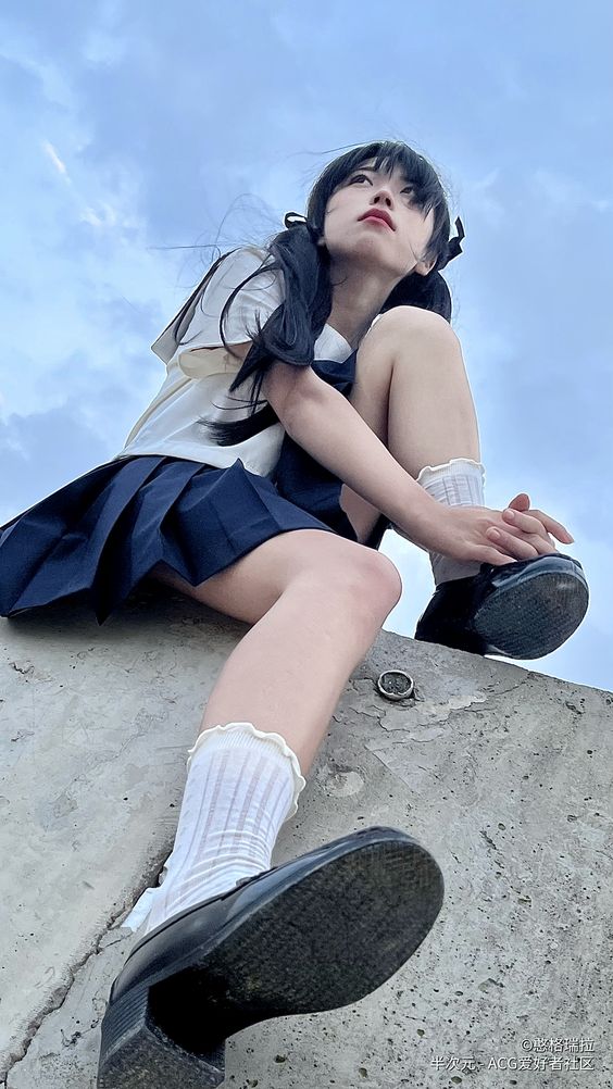 a young woman wearing a school uniform sits on a concrete ledge. she is looking up at the sky, which is mostly blue with some white clouds. she is wearing black shoes and white socks. her hair is styled in pigtails. the image is taken from a low angle.