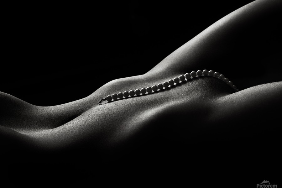 the image is a black and white, closeup photograph of a woman's lower abdomen and torso. the body is positioned lying down, angled slightly, and the lighting is dramatic, using strong shadows and highlights to accentuate the curves of the body.  a strand of pearls rests delicately on the woman's lower abdomen. the overall mood is sensual and intimate, emphasizing the beauty and form of the female body through a minimalist and artistic approach. the dark background further isolates the subject, drawing attention to the textures and contrasts in lighting on the skin.