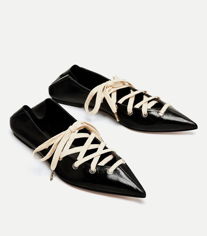 a pair of black leather flats with creamcolored laces are shown in the image. the shoes are pointedtoe and have a minimalist design. they appear to be made of highquality leather and are suitable for both casual and formal occasions.  the laces are tied in a crisscross pattern across the top of the foot. the shoes are positioned on a light gray background. one shoe is slightly angled towards the other.