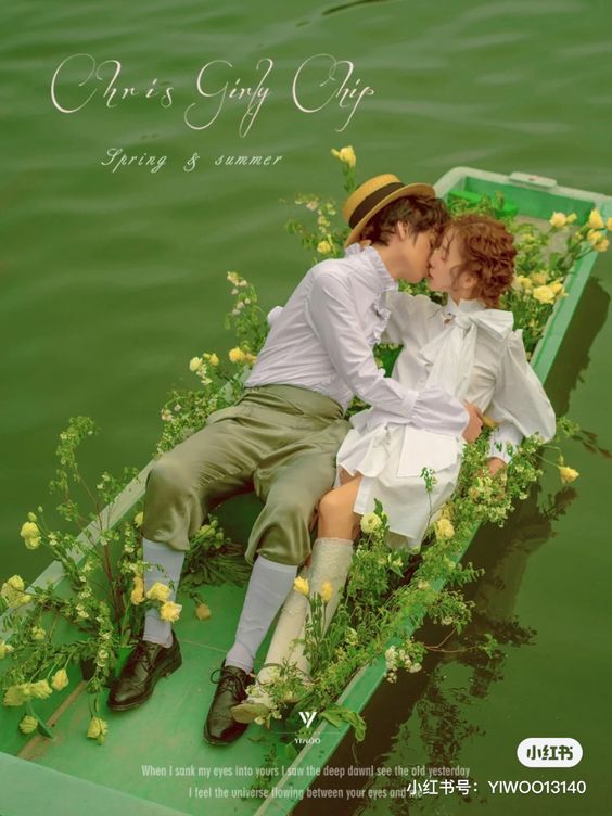 a photo of a couple kissing in a boat filled with yellow roses, floating on a river. the photo is an advertisement for chris giny arip's spring/summer collection. the man is wearing a white shirt, a green velvet suit, and a straw hat, while the woman is wearing a white dress and white socks. the photo has a vintage feel and the text is in both english and chinese.