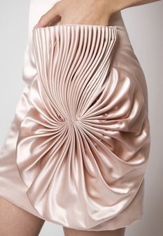 a closeup image of a woman wearing a beautiful pink pleated skirt.  the skirt is made of a soft and silky fabric that drapes beautifully. the pleats are arranged in a pattern that creates a unique and elegant look.  the skirt is very flattering and would be perfect for a special occasion.