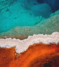 an aerial view of a hot spring with vibrant colors, showing the turquoise water transitioning to orange and white mineral deposits.