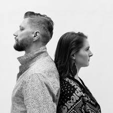 a man and woman stand side by side, their heads turned away from each other, creating