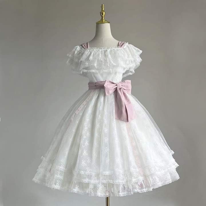 a white lace and tulle dress is shown on a mannequin. the dress has a ruffled offtheshoulder neckline and a flowing skirt with multiple layers of lace and tulle. a pink ribbon is tied around the waist. the dress is elegant and romantic, perfect for a party or special occasion.