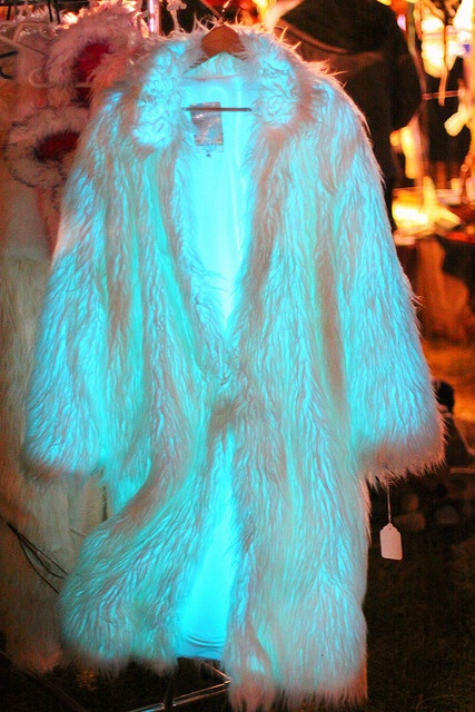 a white fur coat is glowing a bright blue color, highlighting the soft, fluffy texture of the fabric. the coat is hanging on a rack in a dimly lit room, and its glow is casting a blue hue on the surrounding area. the garment appears to be made of a highquality material, making it look both fashionable and comfortable. the coat is a statement piece that would be perfect for a night out or a special occasion.