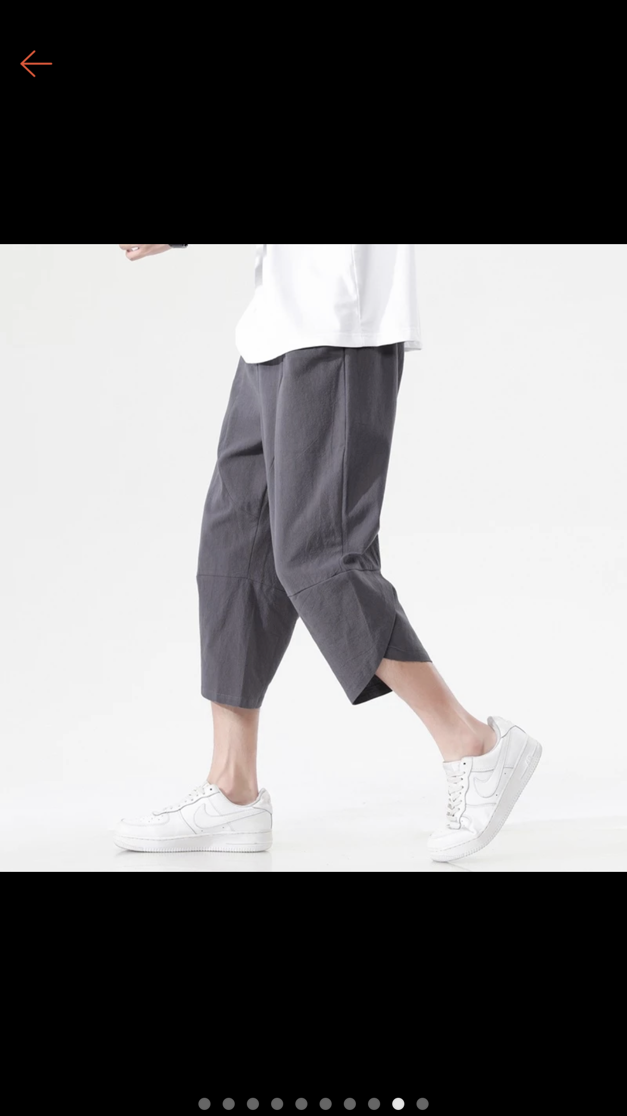 a man wearing grey cropped pants and white sneakers stands against a white background. he is wearing a white shirt that is partially visible. his pose suggests movement, as if he is about to take a step. the image is welllit, showcasing the details of the clothing and the model's stance. the background is plain, drawing focus to the outfit and the model.