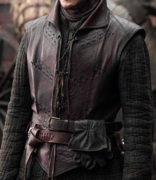 the image shows a man's torso and upper body, clad in a medieval or fantasystyle outfit. he wears a dark brown leather vest with decorative stitching and a high collar. underneath the vest is a quilted jacket or shirt. a leather belt is cinched around his waist, with a pair of black leather gloves attached to it. the overall aesthetic suggests a historical or fantasy character.