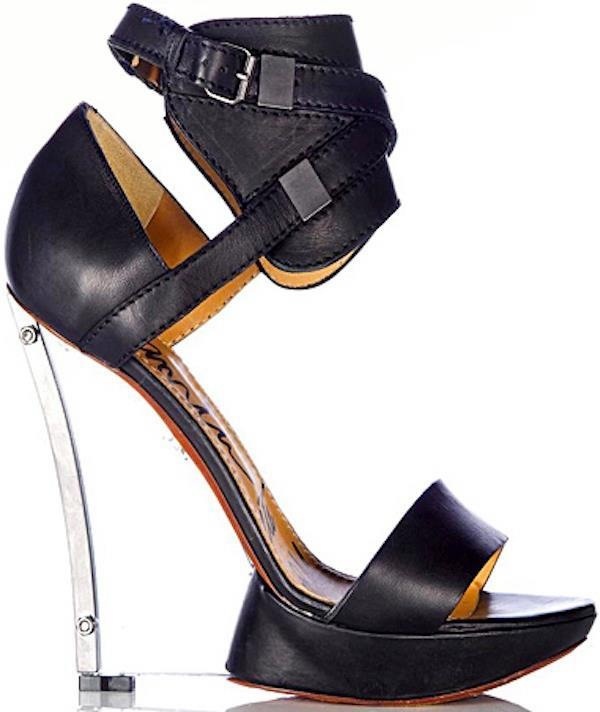 a closeup shot of a pair of black leather women's sandals with a unique design.  the sandals feature a high platform, a clear metallic wedge heel, an ankle strap with buckle detailing, and a black leather upper. the shoes are positioned on a white background, showcasing their design details.