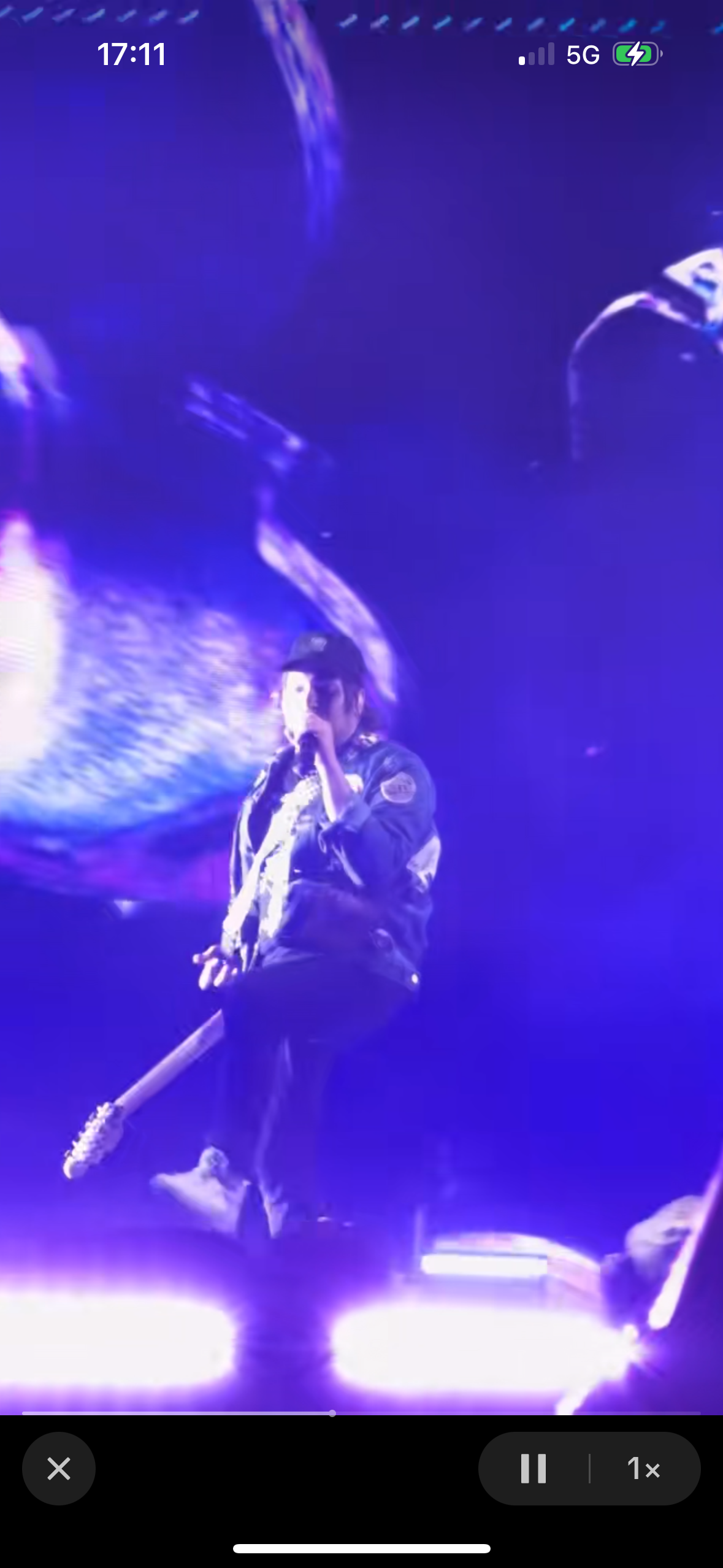 a musician performs on stage at a concert, bathed in purple light, with an audience cheering in the background. the musician is holding a microphone and performing to a lively crowd, showcasing their passion for music. the energy of the concert is palpable, with the vibrant stage lights and the excited cheers of the audience adding to the atmosphere.