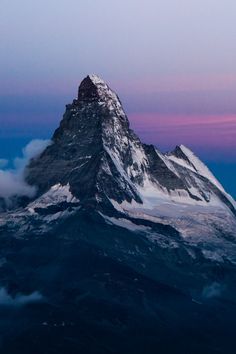 an aerial view of a snowcapped mountain peak against a twilight sky. the mountain is partially obscured by clouds, and the sky is a mix of purple, blue, and pink hues.