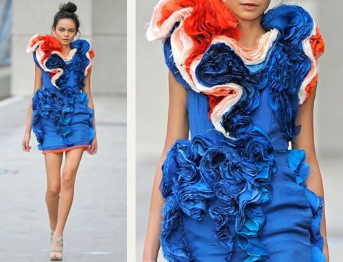this image showcases a fashion model in a stunning blue, white, and red dress with a dramatic, ruffled design. the dress features multiple layers of ruffles that cascade from the shoulders to the hemline, creating a striking and eyecatching silhouette. the model's confident pose and the overall aesthetic of the outfit convey a sense of high fashion and avantgarde style. the image captures the artistry and creativity of the fashion world, showcasing a truly unique and memorable garment.