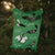 he image shows a blurry, closeup view of a green bag or piece of fabric hanging outdoors amongst trees. the bag has a design or pattern that is not fully clear due to the blur.  the background is dark and mostly out of focus, suggesting a natural setting. sunlight is visible in the upperleft corner. the overall feel is slightly mysterious and environmental.
