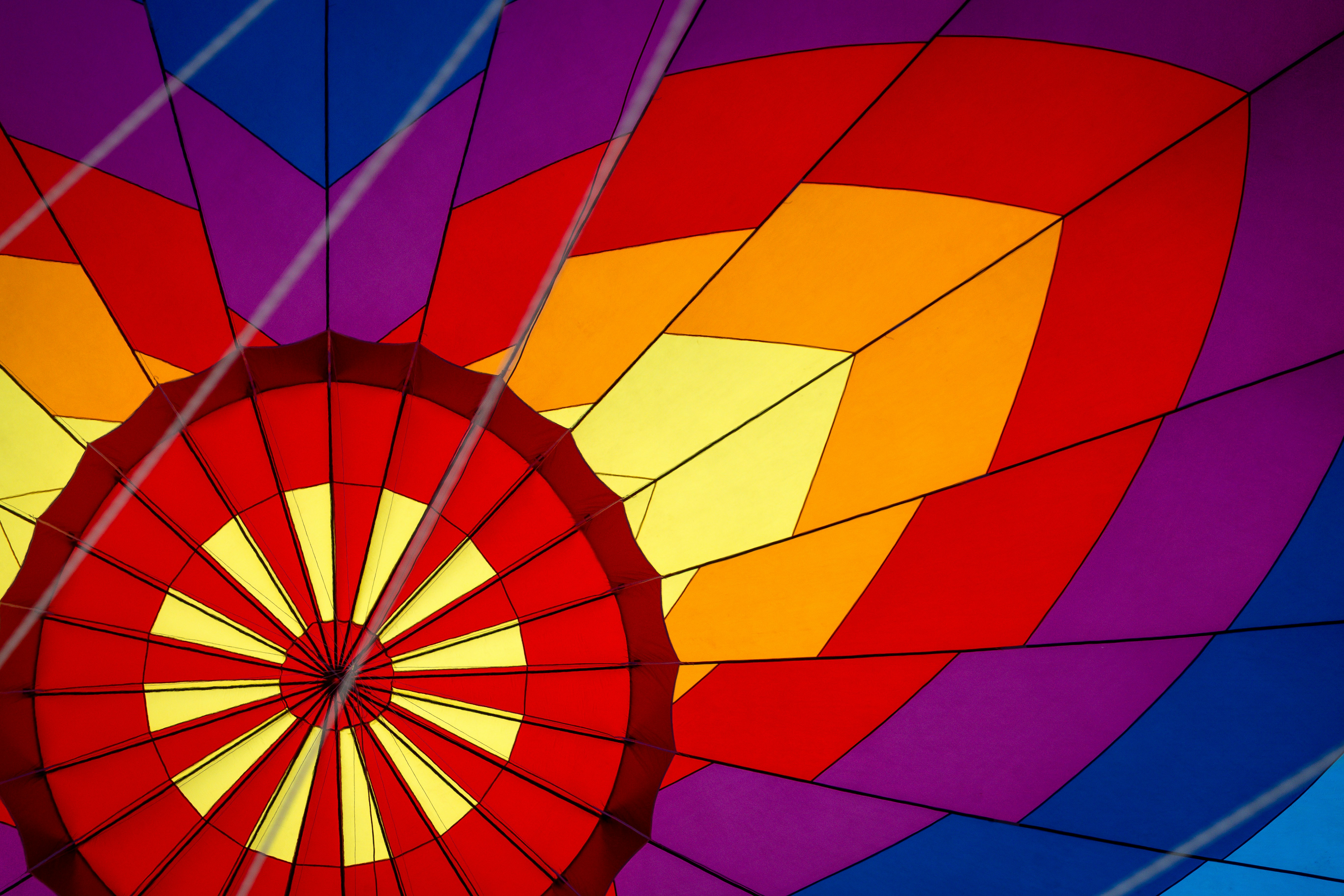 a closeup shot of the inside of a colorful hot air balloon, capturing the vibrant and intricate patterns of its fabric. the balloon is adorned with red, yellow, orange, purple, and blue stripes and panels, creating a captivating geometric abstract design. the image highlights the intricate details of the balloon's construction and its striking visual appeal.
