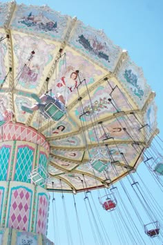 a colorful carousel with intricate designs and hanging seats under a bright blue sky. the carousel is adorned with whimsical designs and vibrant colors, adding to its charm and creating a festive atmosphere. the sun shines brightly, casting a warm glow on the scene. the image captures the joy and excitement of a carnival or amusement park, evoking feelings of nostalgia and carefree fun.
