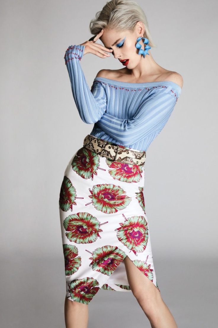 a beautiful woman is wearing a blue offtheshoulder sweater, floral skirt, and a snake skin belt. she has blonde hair, blue eyeshadow, and  red lipstick.