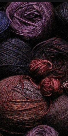 a closeup image of a variety of yarn balls in shades of purple, red, and brown, with the texture of the yarn clearly visible. the image is focused on the yarn balls, showing the details of their weave and texture. the balls are arranged in a messy pile, suggesting a collection of crafting materials.