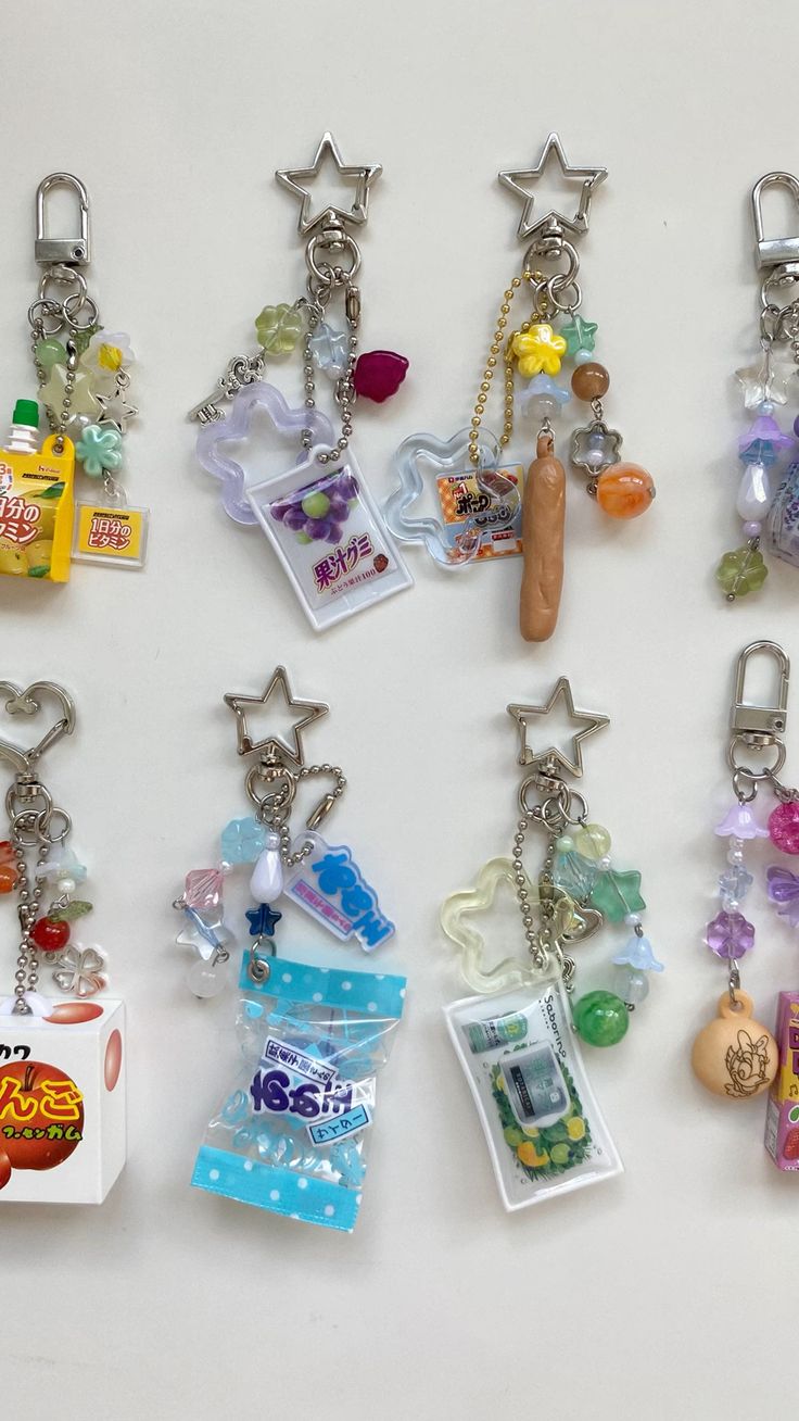 the image shows a closeup of several colorful keychains hanging against a white background. the keychains feature starshaped clasps and various charms, including miniature food items like candy, gummies, and snacks. they are embellished with beads and other decorative elements.