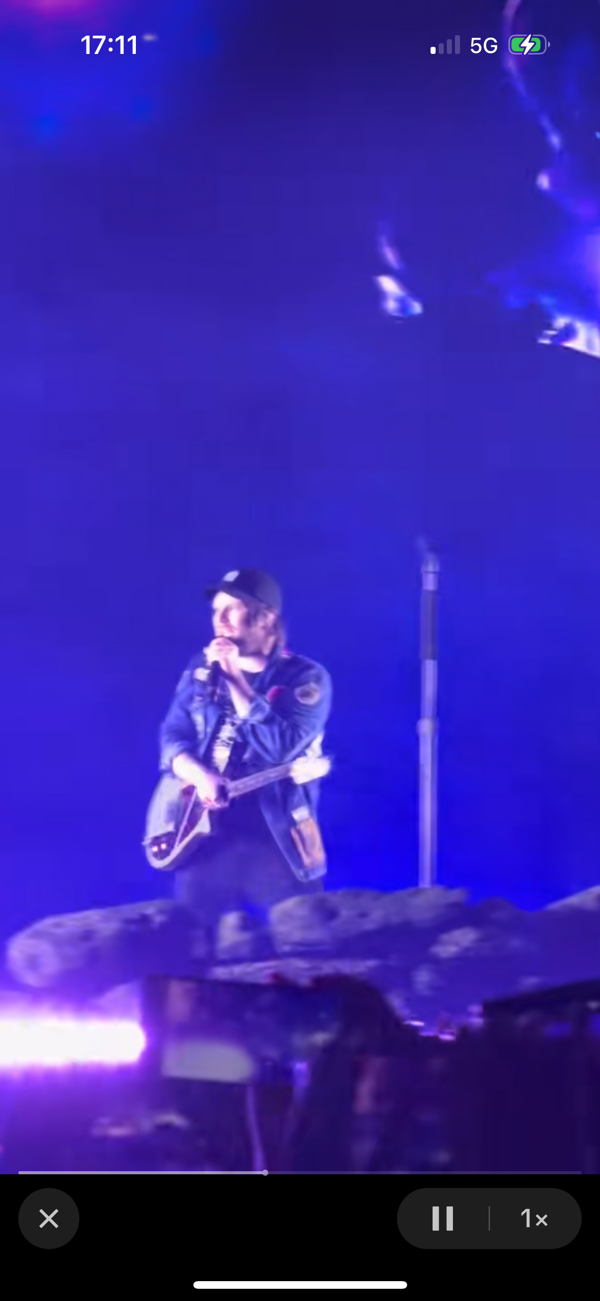 a musician is playing a guitar on stage during a concert. the stage is lit up with purple and blue lights and there is a crowd of people in the background. the musician is silhouetted against the lights. the image is captured in a dark environment, capturing the energy and passion of a live concert.