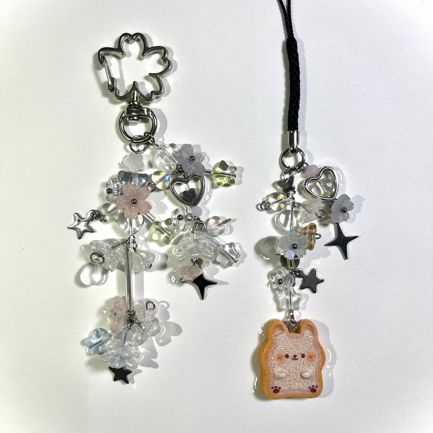 two keychains with various beads, charms, and pendants are displayed. one has a metal flower clip at the top and a variety of floral and star charms with beads. the second keychain has a black cord with similar flower and star charms but ends with a bunnyshaped pendant.