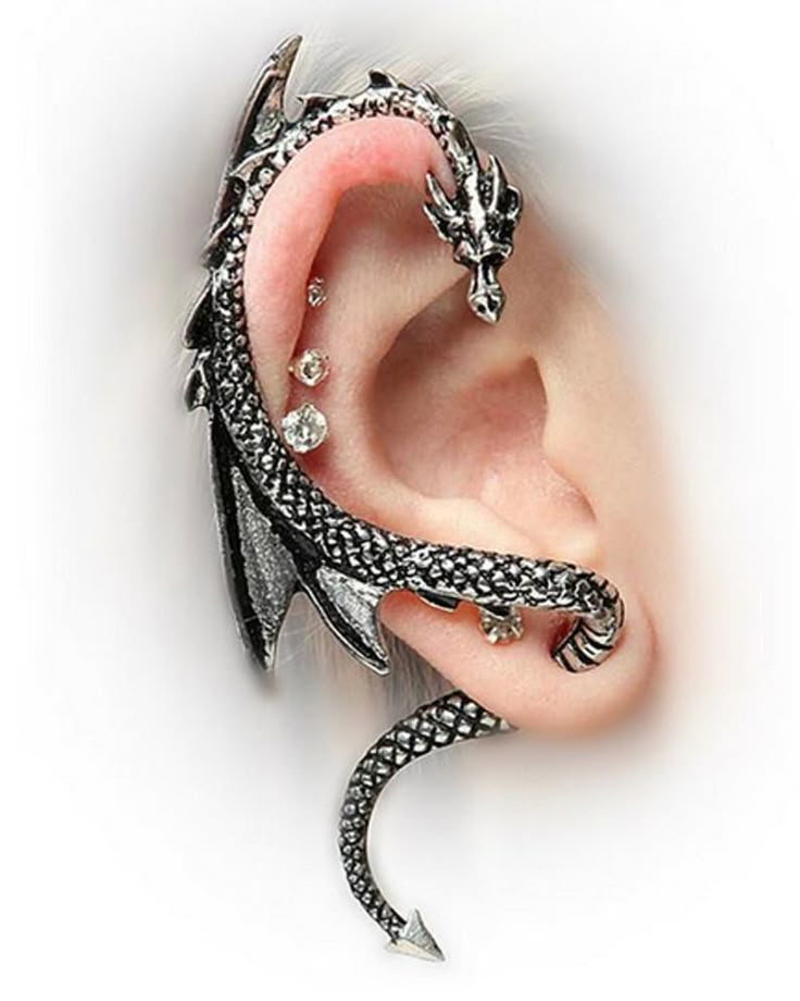 a closeup image shows an ear adorned with a silvercolored dragon ear cuff. the dragon wraps around the ear, with its head at the top and its tail curving down near the earlobe. there are also a few piercings visible on the ear. the ear cuff has a detailed, gothicinspired design with wings and scales.